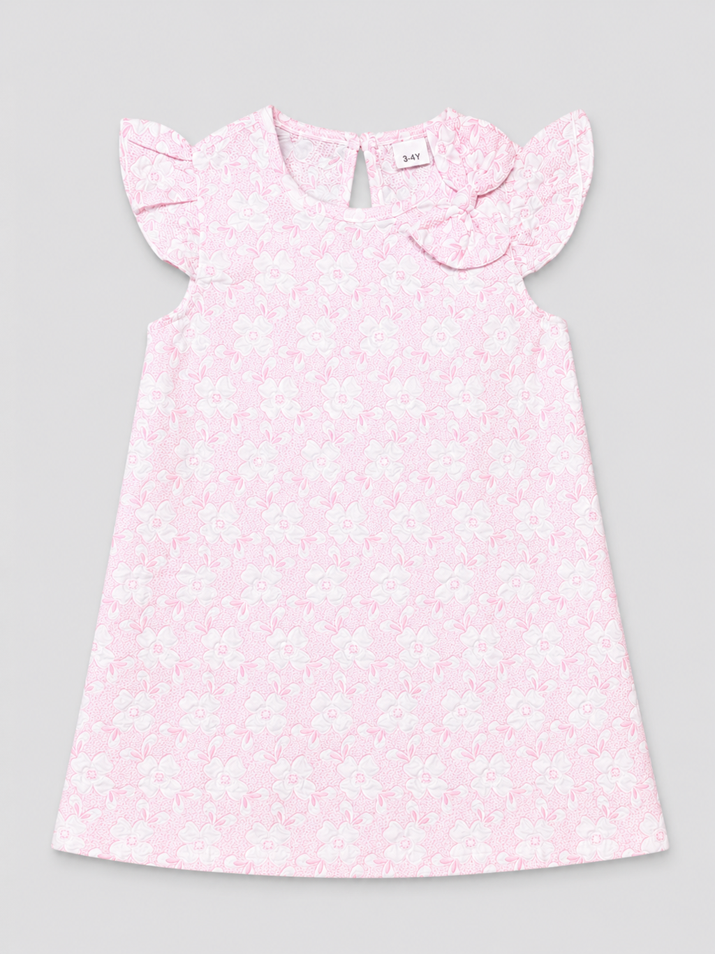 A light pink sleeveless dress for a toddler girl, featuring a delicate white floral pattern, ruffled cap sleeves, and a matching fabric bow on the chest, shown flat on a neutral gray background.