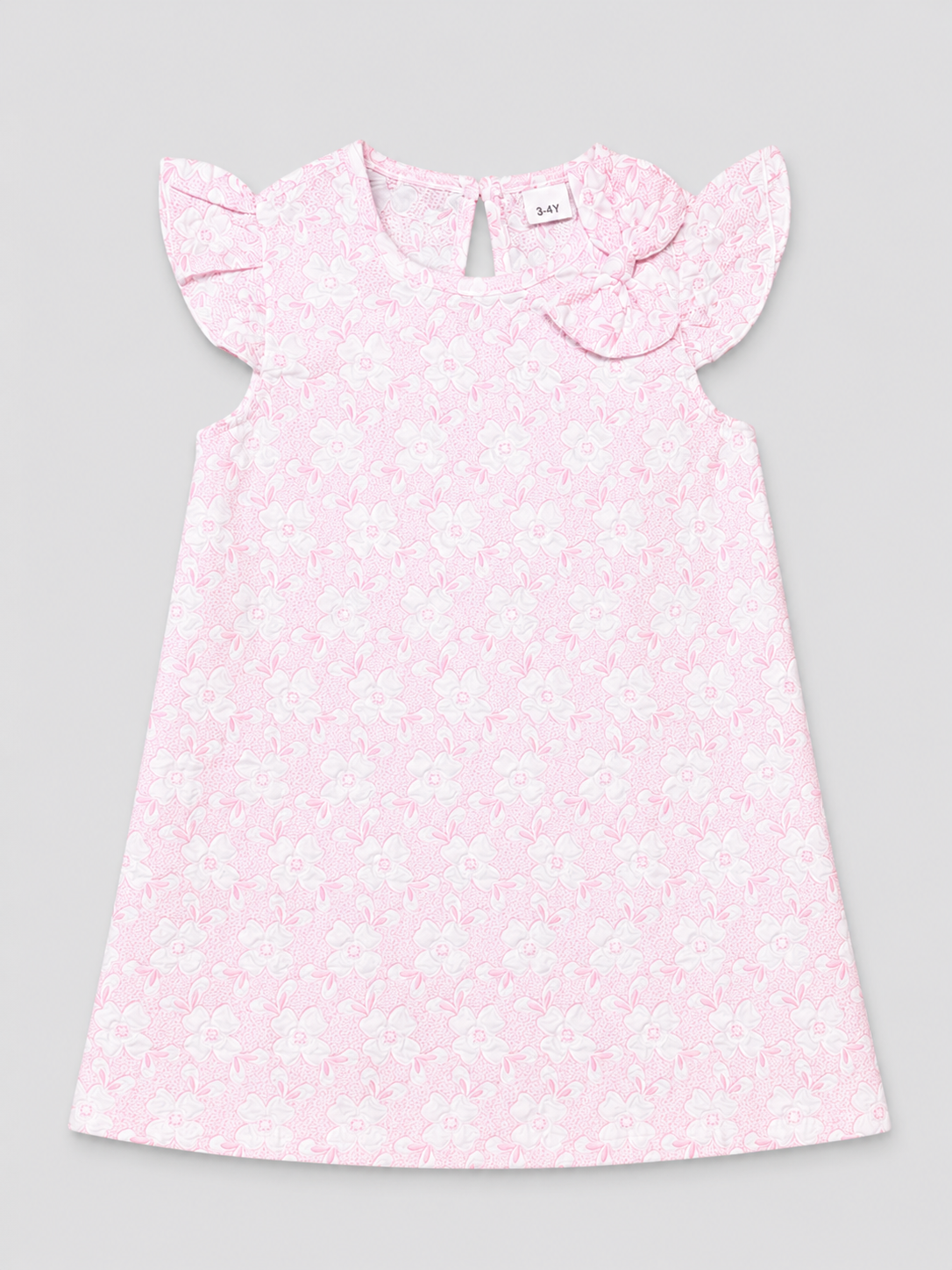 A light pink sleeveless dress for a toddler girl, featuring a delicate white floral pattern, ruffled cap sleeves, and a matching fabric bow on the chest, shown flat on a neutral gray background.