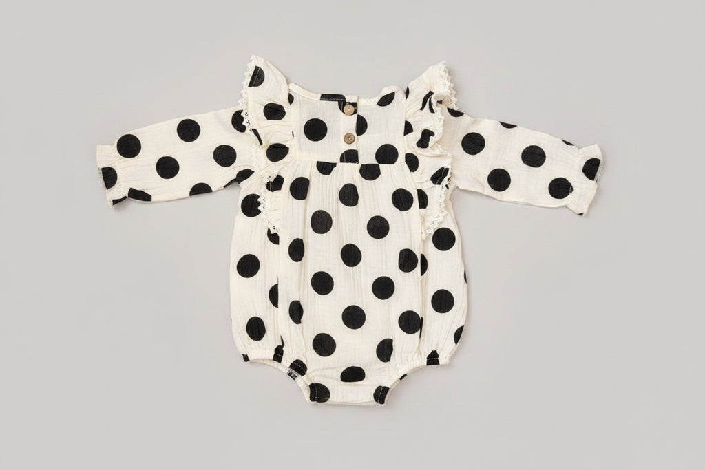 Baby girl black and white polka dot bubble romper featuring lace-trimmed ruffles, long sleeves, and a soft cotton muslin fabric. A timeless boutique outfit for everyday wear, family photos, and special occasions.