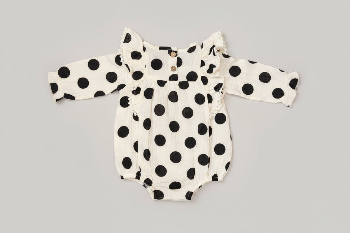 Baby girl black and white polka dot bubble romper featuring lace-trimmed ruffles, long sleeves, and a soft cotton muslin fabric. A timeless boutique outfit for everyday wear, family photos, and special occasions.