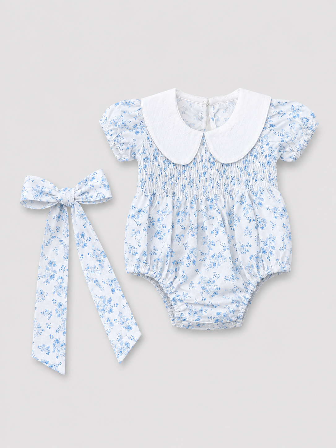 Baby girls white and light blue floral smocked romper with Peter Pan collar and matching floral bow, front view, size 1–3M.