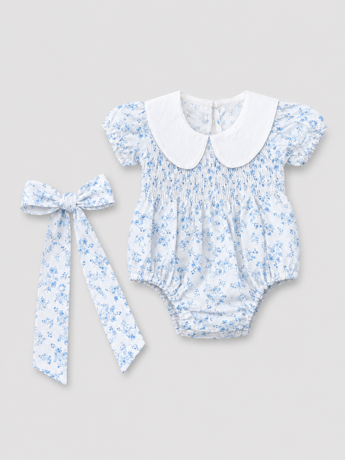 Baby girls white and light blue floral smocked romper with Peter Pan collar and matching floral bow, front view, size 1–3M.