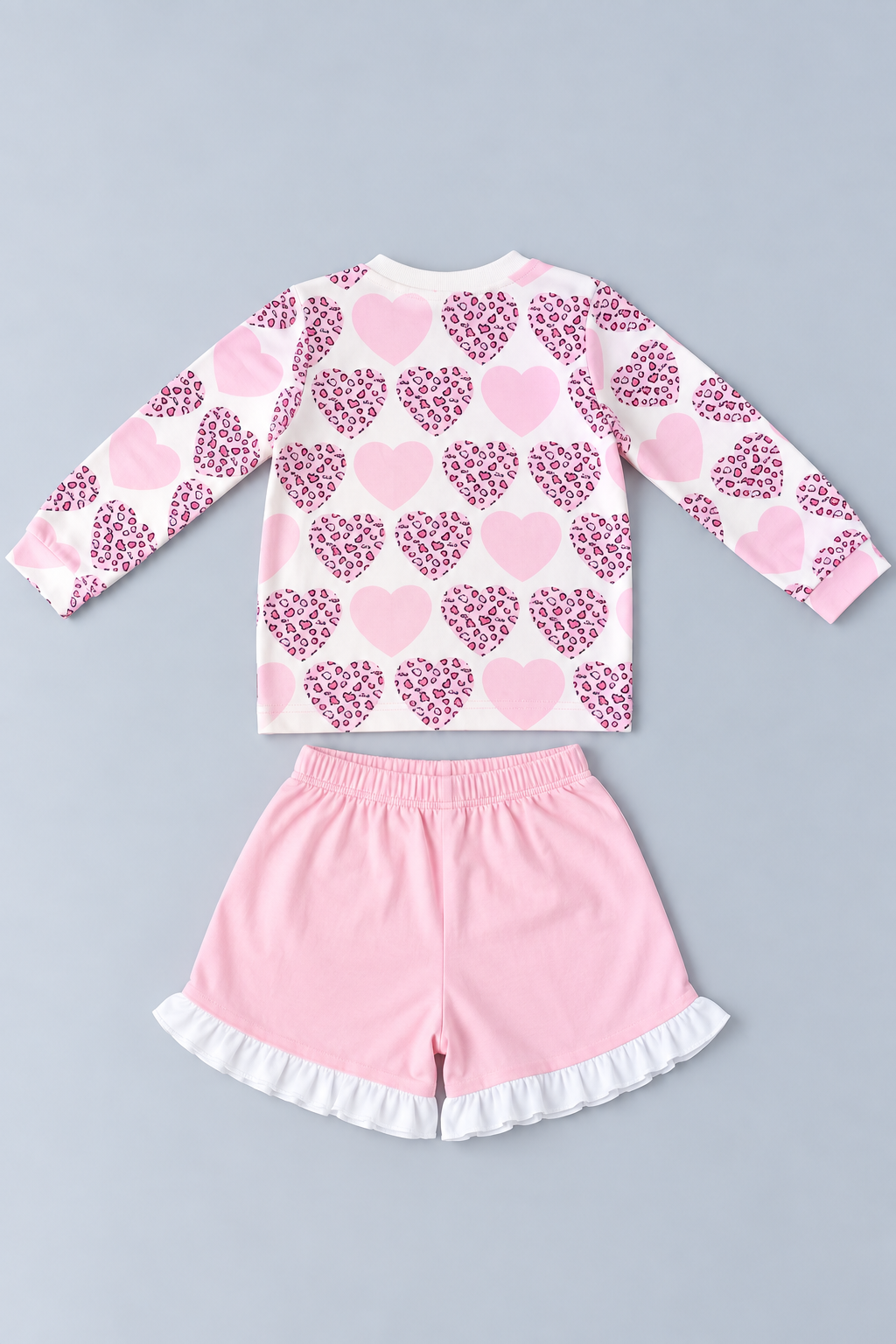 Back view of girls pink heart-print long-sleeve top and coordinating pink shorts with white ruffle hems.