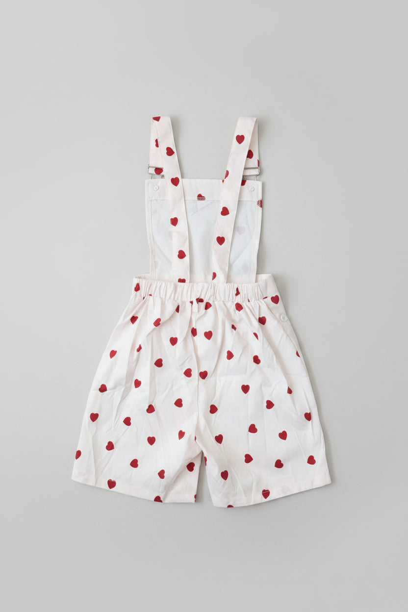 Adorable girls 2-piece suspender shorts set featuring a red ribbed ruffle top and white heart-print overalls. Perfect for Valentine's Day, parties, family photos, and everyday boutique style.
