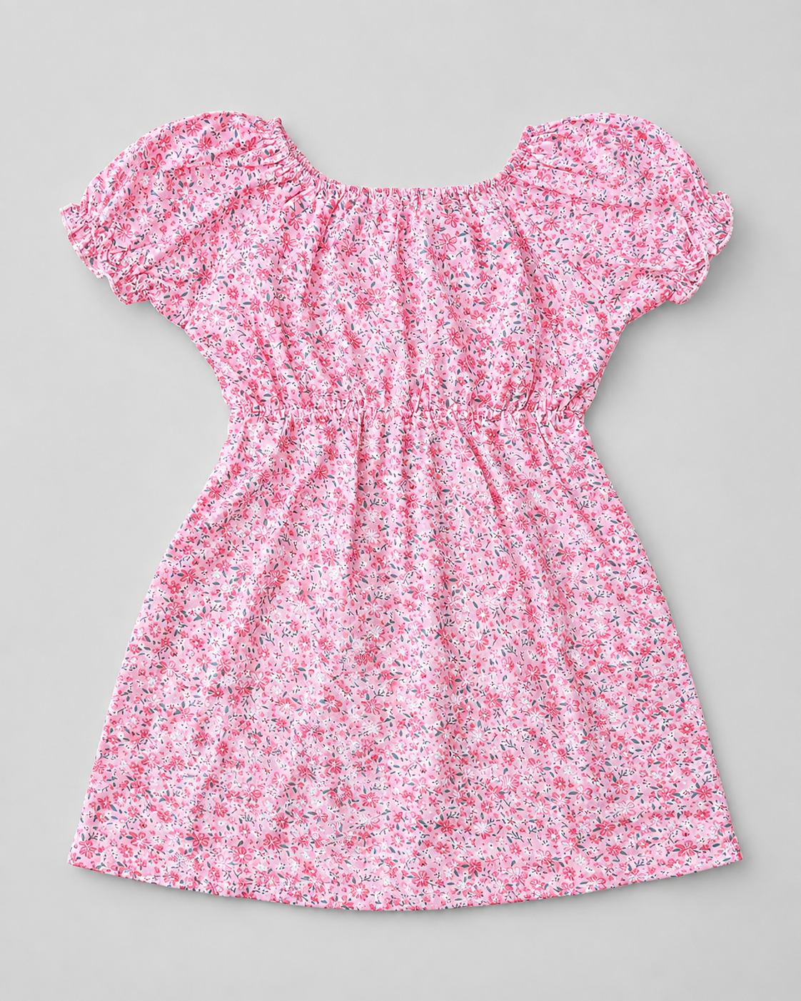 A pink short-sleeve babydoll dress with a dense small floral print, featuring a smocked bodice and ruffled shoulders, laid flat on a neutral gray background.