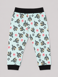 A pair of children's jogger pants with a light blue background, featuring a repeating pattern of black and yellow guitars, pink flowers, and gray diamond shapes. The pants have black elastic waistbands and black ribbed ankle cuffs.