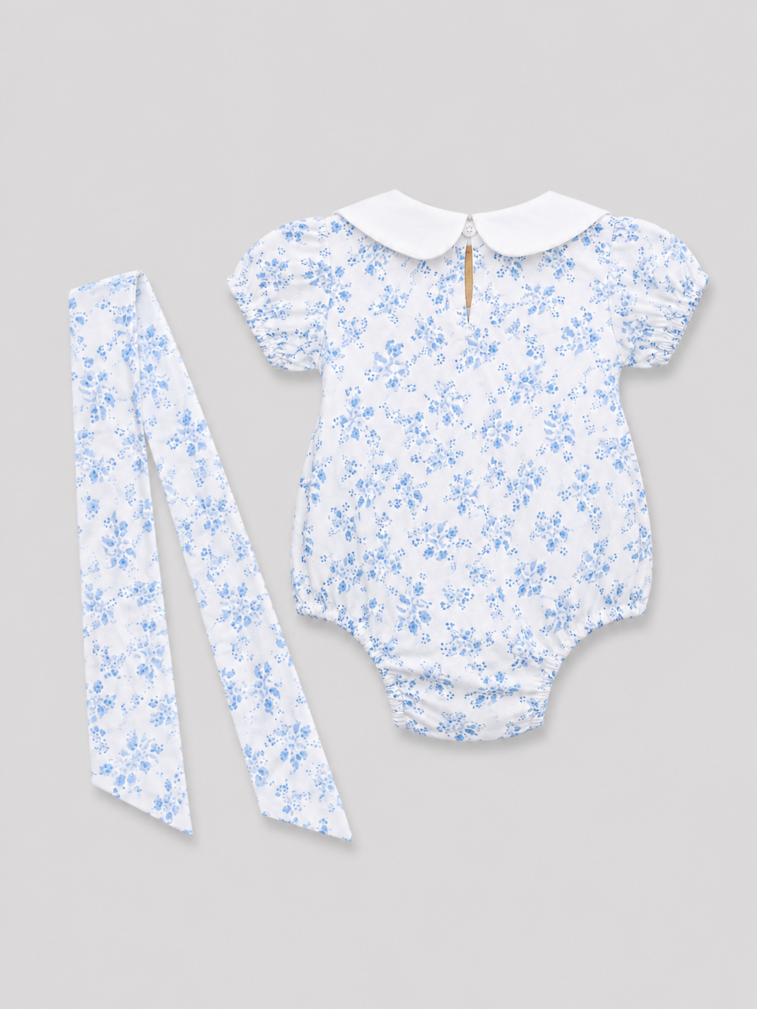 Baby girls white and light blue floral romper with Peter Pan collar, back keyhole button closure, and matching floral sash, back view, size 1–3M.