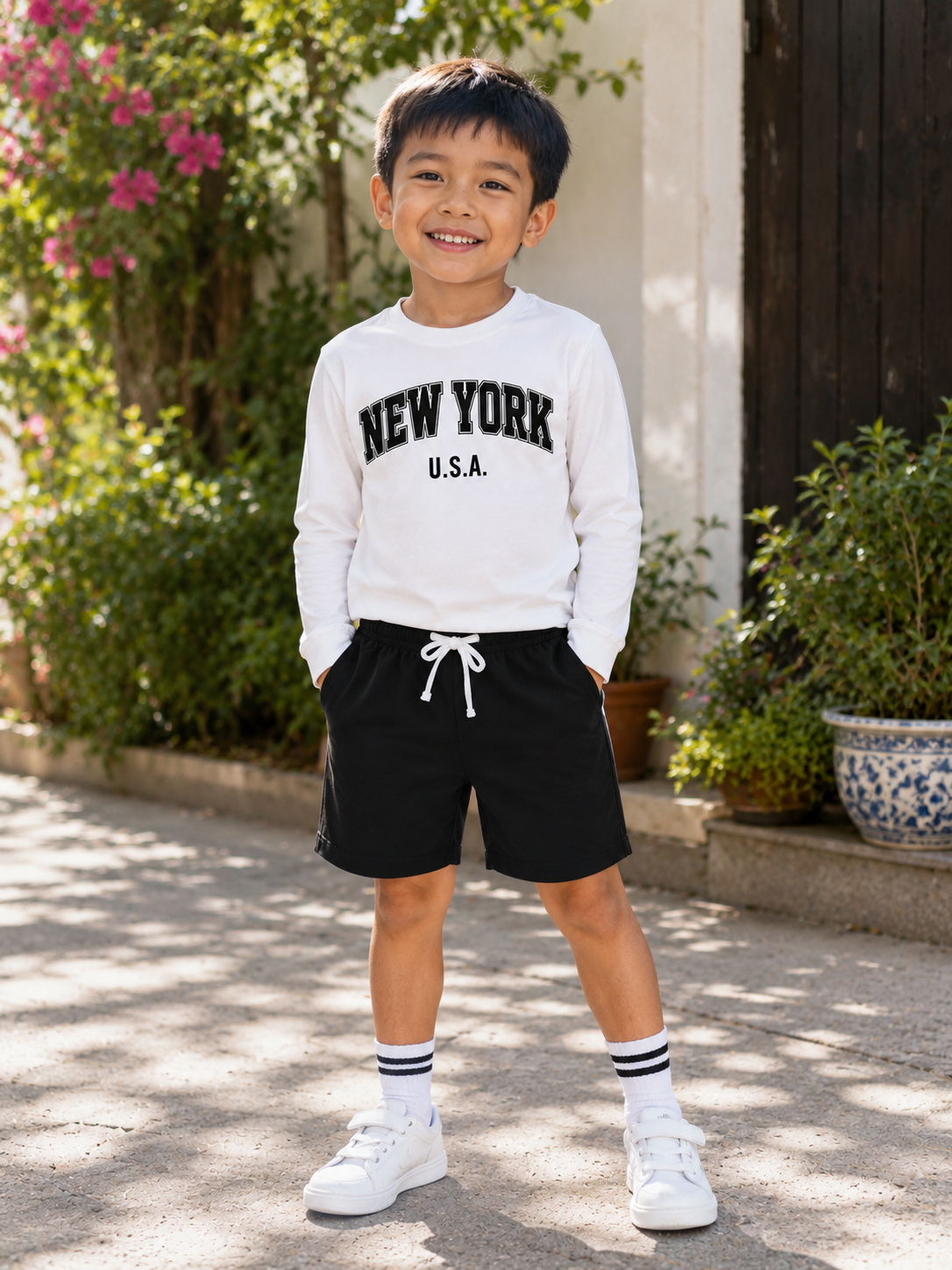 A young boy stands outdoors wearing a white long-sleeve crewneck sweatshirt with 'NEW YORK U.S.