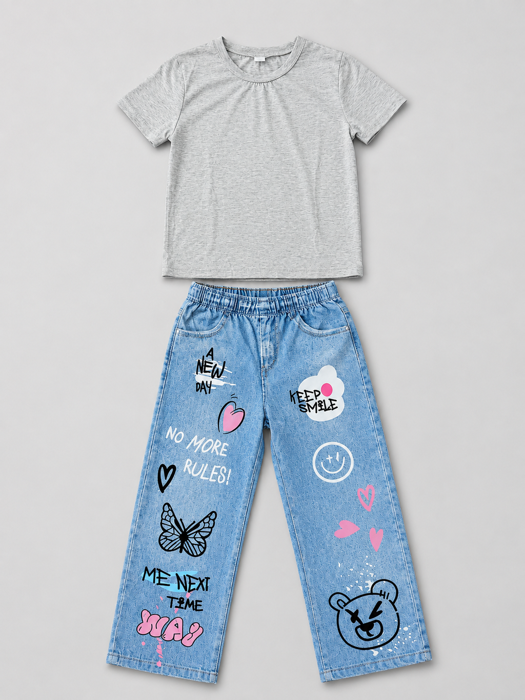 Shop this stylish girls’ two-piece outfit featuring a gray graphic T-shirt and light blue wide-leg pants with playful graffiti-inspired graphics, hearts, butterflies, and fun character details.