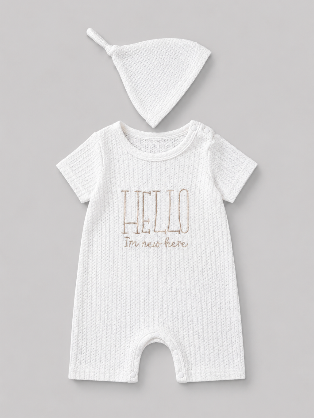 Shop this sweet white baby romper and matching knot hat set featuring textured fabric and an embroidered “Hello I’m new here” message. Perfect for newborn photos, coming-home outfits, and baby gifts.