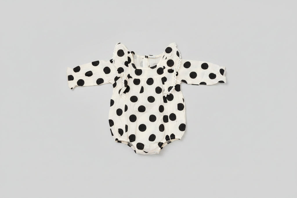 Baby girl black and white polka dot bubble romper featuring lace-trimmed ruffles, long sleeves, and a soft cotton muslin fabric. A timeless boutique outfit for everyday wear, family photos, and special occasions.