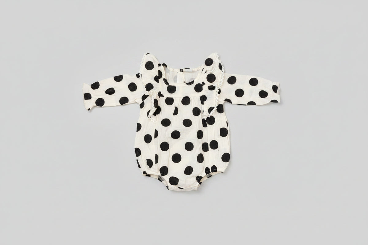 Baby girl black and white polka dot bubble romper featuring lace-trimmed ruffles, long sleeves, and a soft cotton muslin fabric. A timeless boutique outfit for everyday wear, family photos, and special occasions.
