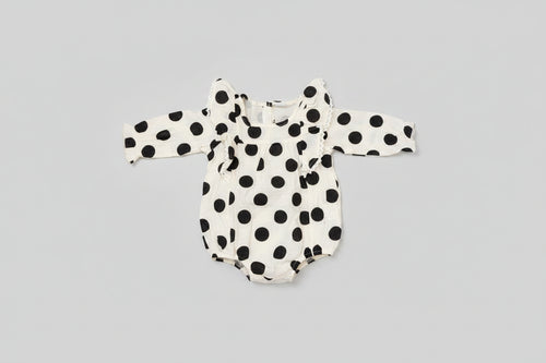Baby girl black and white polka dot bubble romper featuring lace-trimmed ruffles, long sleeves, and a soft cotton muslin fabric. A timeless boutique outfit for everyday wear, family photos, and special occasions.