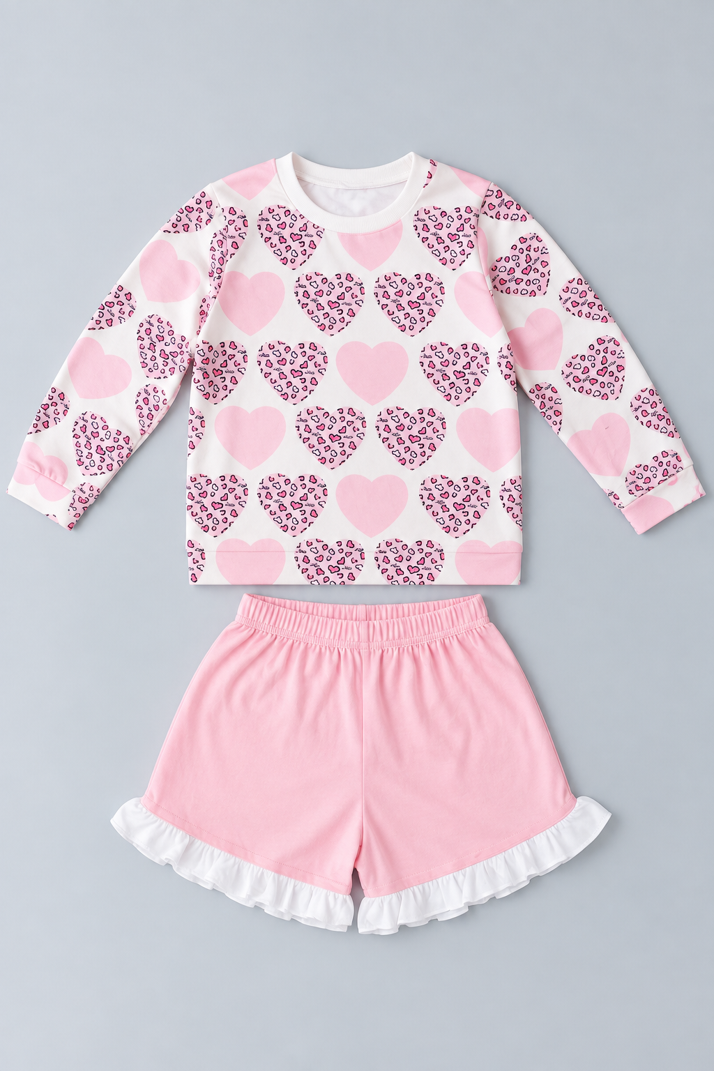 Girls pink and white two-piece outfit with long-sleeve leopard heart-print top and pink shorts with white ruffle trim.
