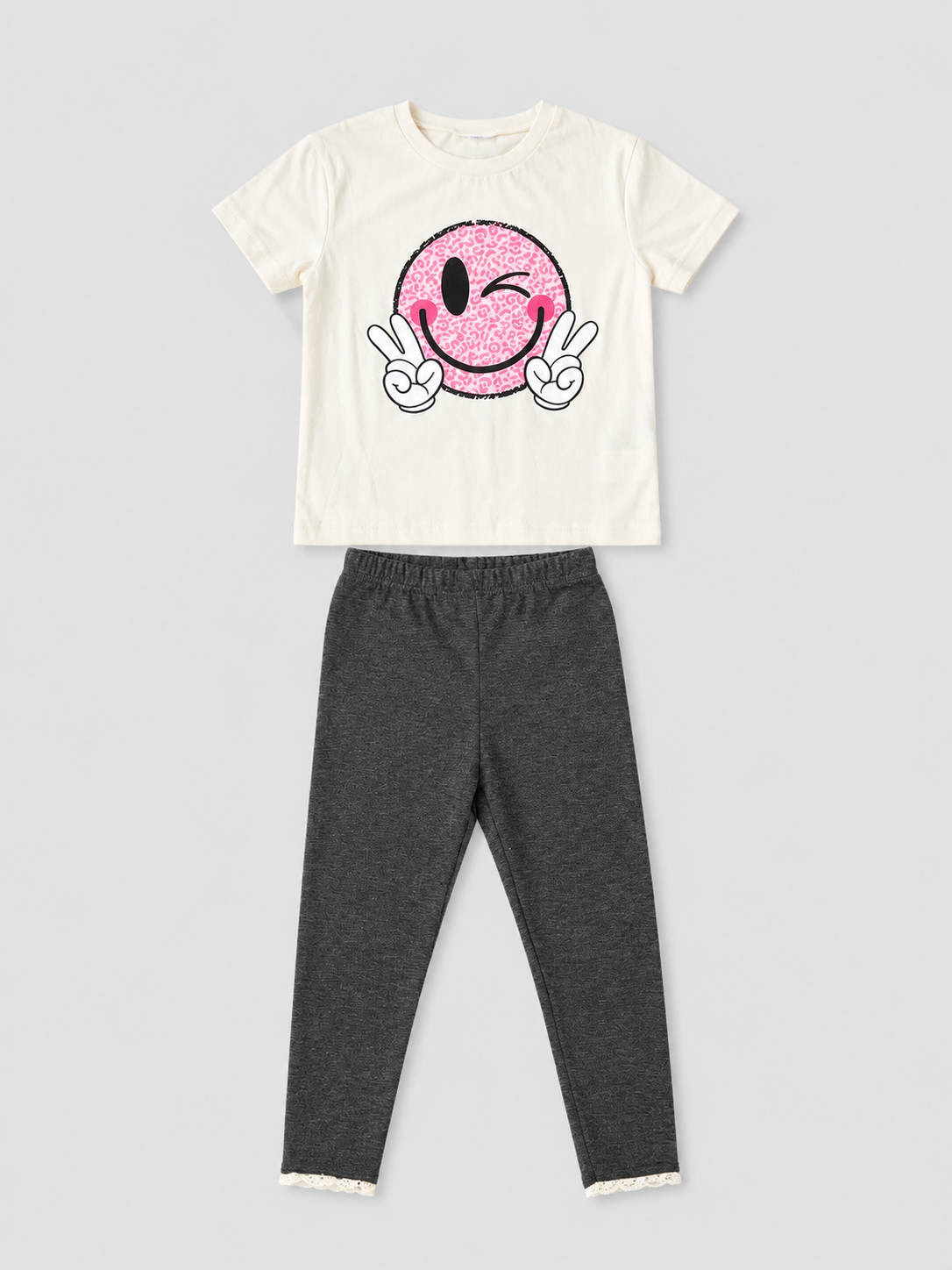 Girls ivory T-shirt with pink winking smiley face graphic and charcoal gray lace-trim leggings two-piece outfit, front view, size 4Y.