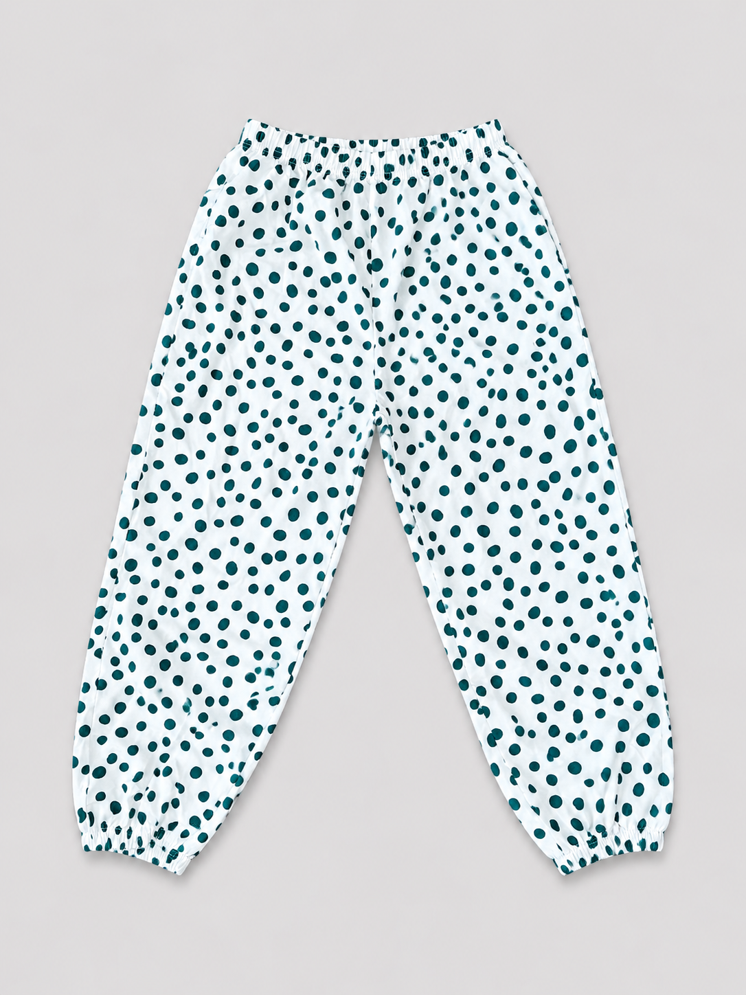 Girls white jogger pants with teal polka dot print, elastic waistband, and gathered ankle cuffs, front view, size 8–10Y.