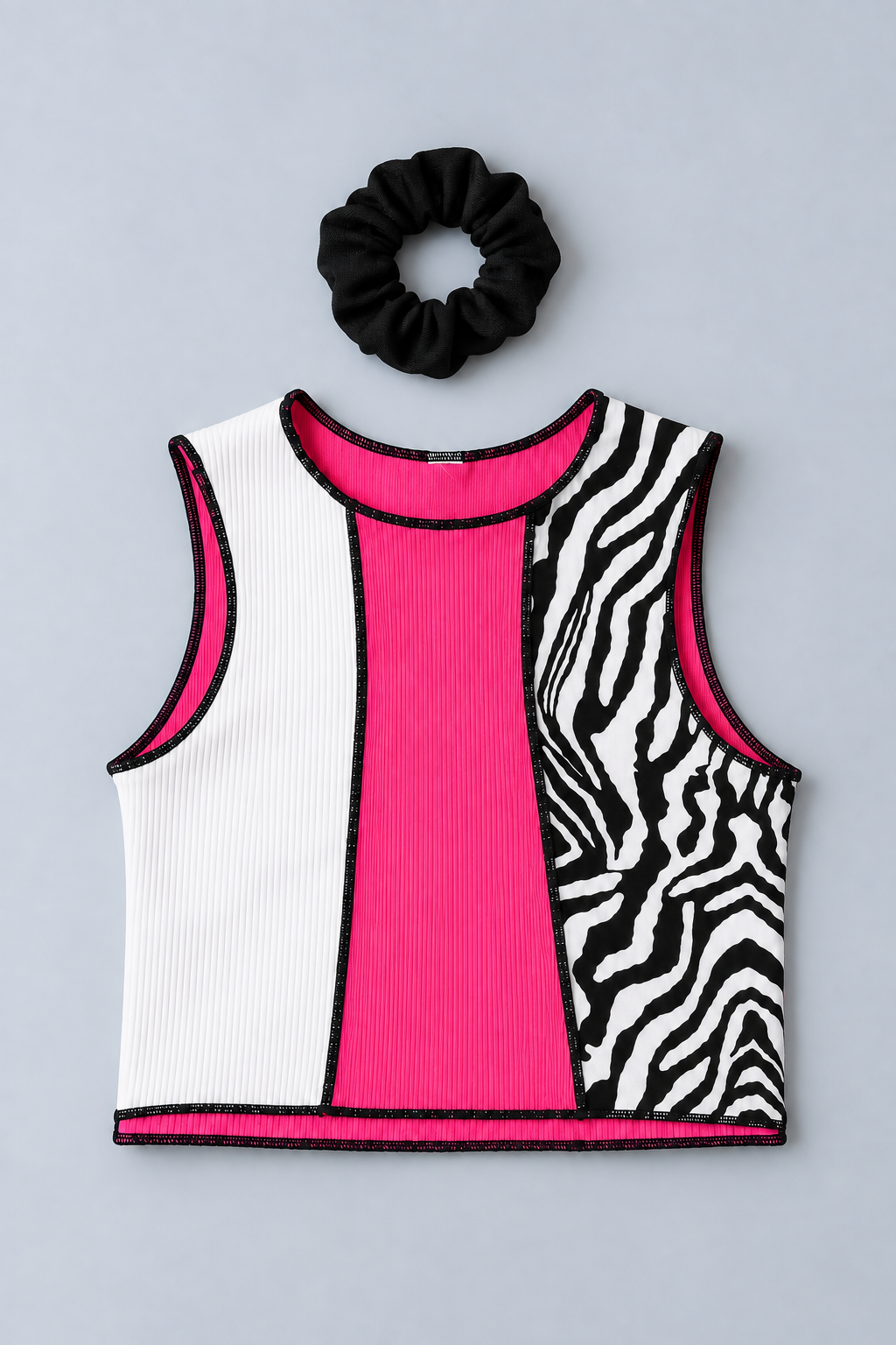 A sleeveless crop top with a color-blocked design featuring white ribbed knit, bright pink ribbed knit, and black-and-white zebra print panels, styled with a black scrunchie.