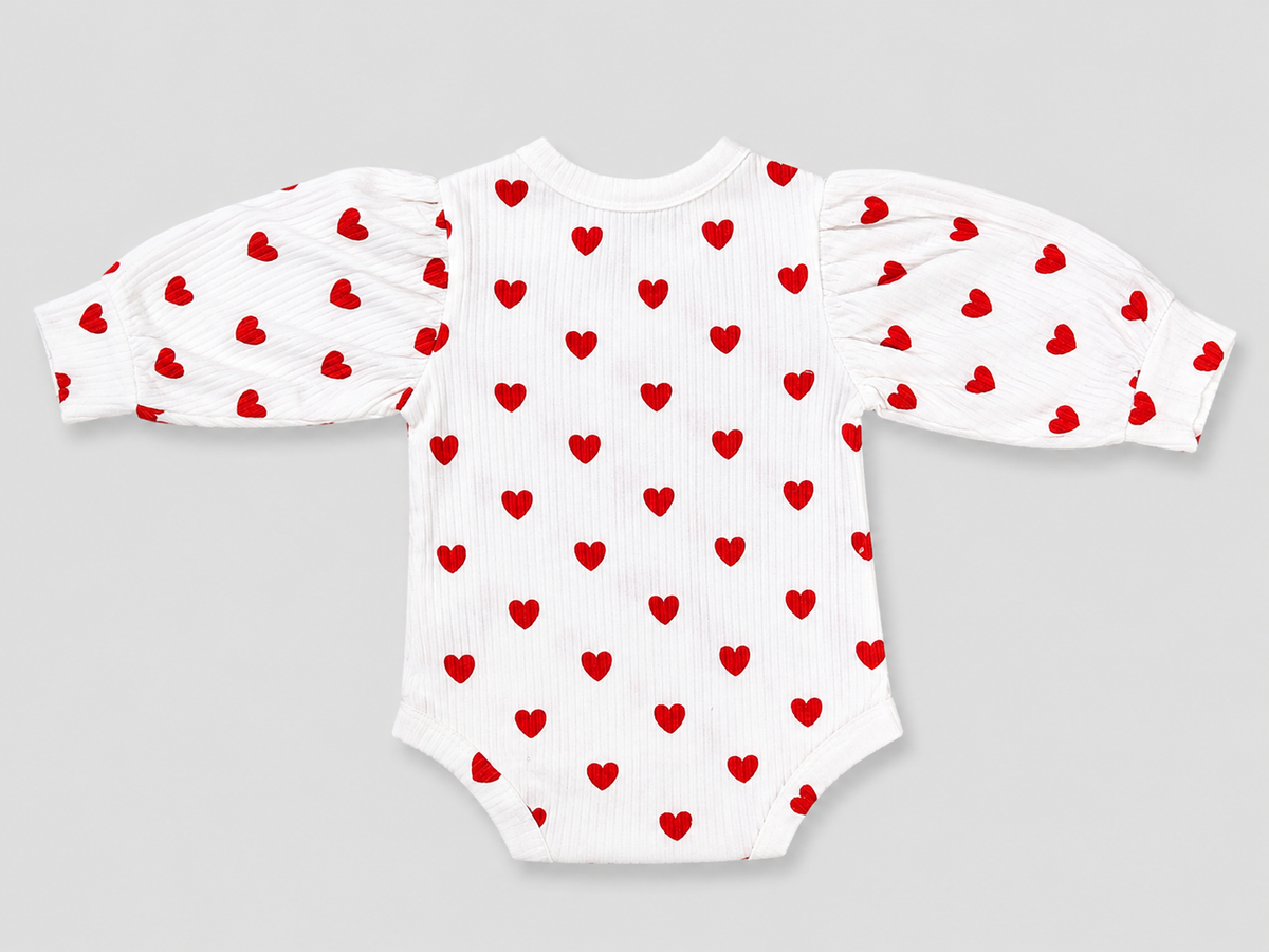 A white long-sleeve baby bodysuit with red heart patterns on the body and sleeves, featuring puffed sleeves and a ribbed texture, shown on a neutral gray background.