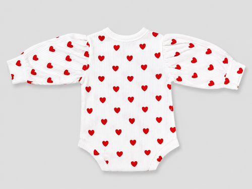 A white long-sleeve baby bodysuit with red heart patterns on the body and sleeves, featuring puffed sleeves and a ribbed texture, shown on a neutral gray background.