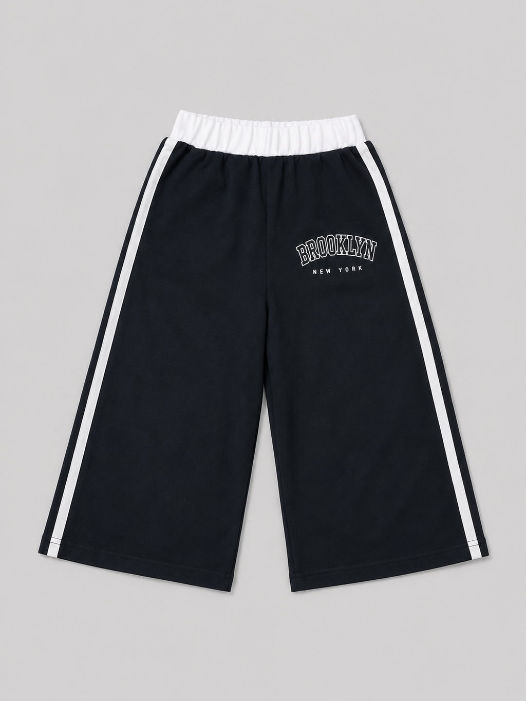 Black athletic shorts featuring white side stripes, an elastic waistband, and a “Brooklyn New York” graphic. A versatile choice for school, sports, playtime, and everyday casual wear.