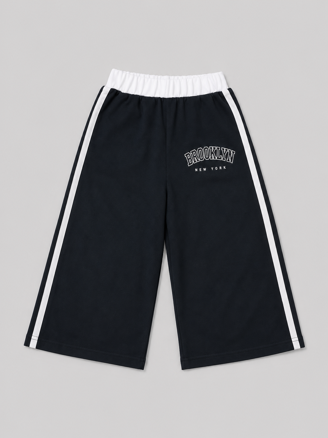 Black athletic shorts featuring white side stripes, an elastic waistband, and a “Brooklyn New York” graphic. A versatile choice for school, sports, playtime, and everyday casual wear.