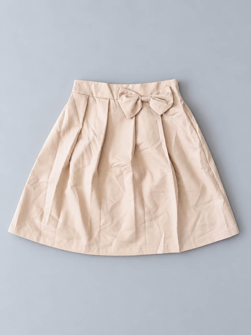 Girls beige pleated skirt with decorative bow and flared silhouette