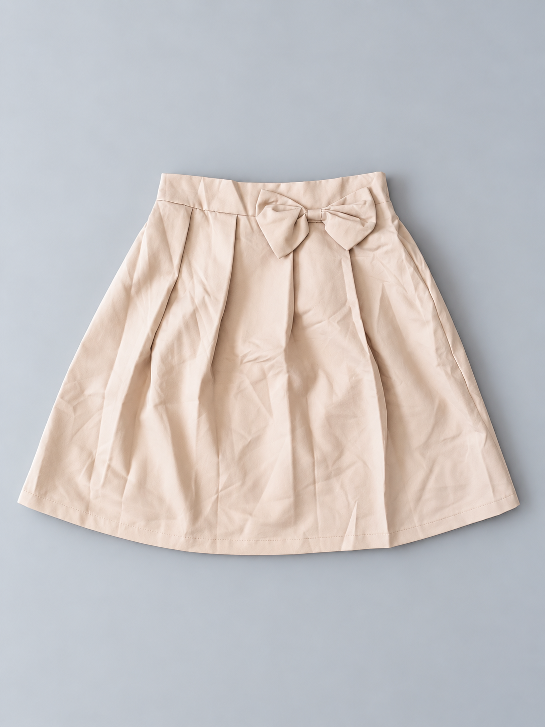 Girls beige pleated skirt with decorative bow and flared silhouette